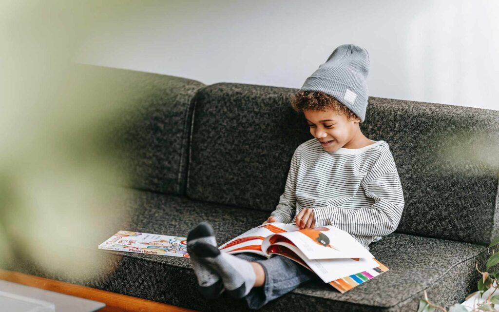 young boy sitting on sofa looking at children magazine