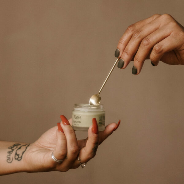 cosmetic spatula inserted in cosmetic jar held by hand with long painted nails