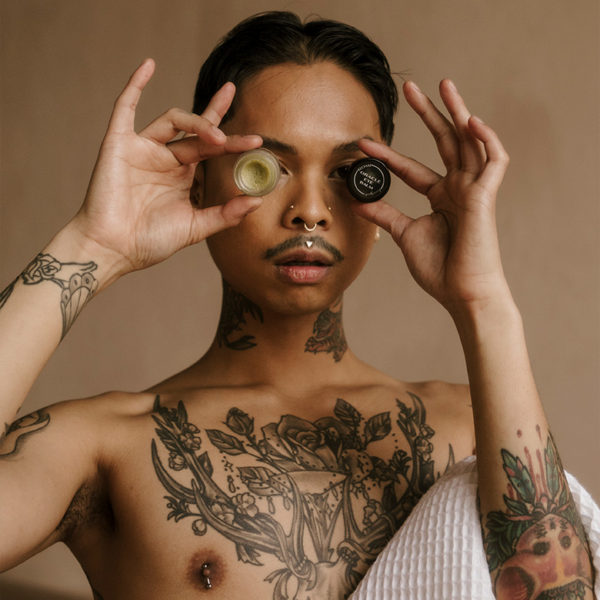 tattooed man posing with eye balm jar and lid covering his eyes