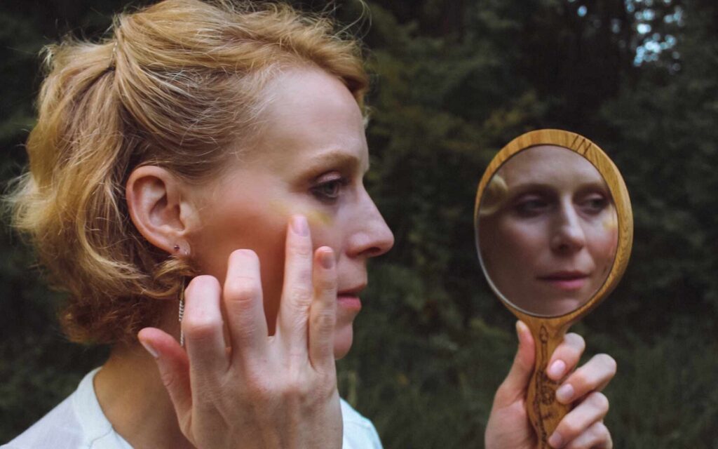 woman applying eye balm while holding a wooden handle mirror