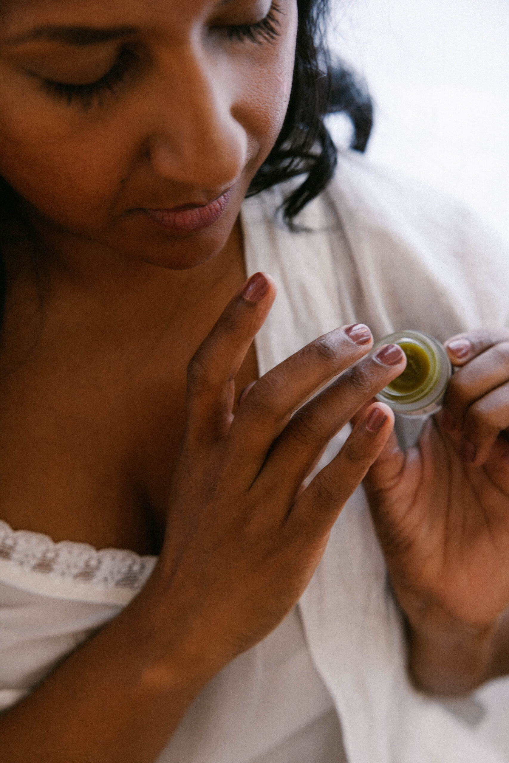 Someone applying Oracle Eye Balm with their ring finger in warm morning light, unhurried and present.