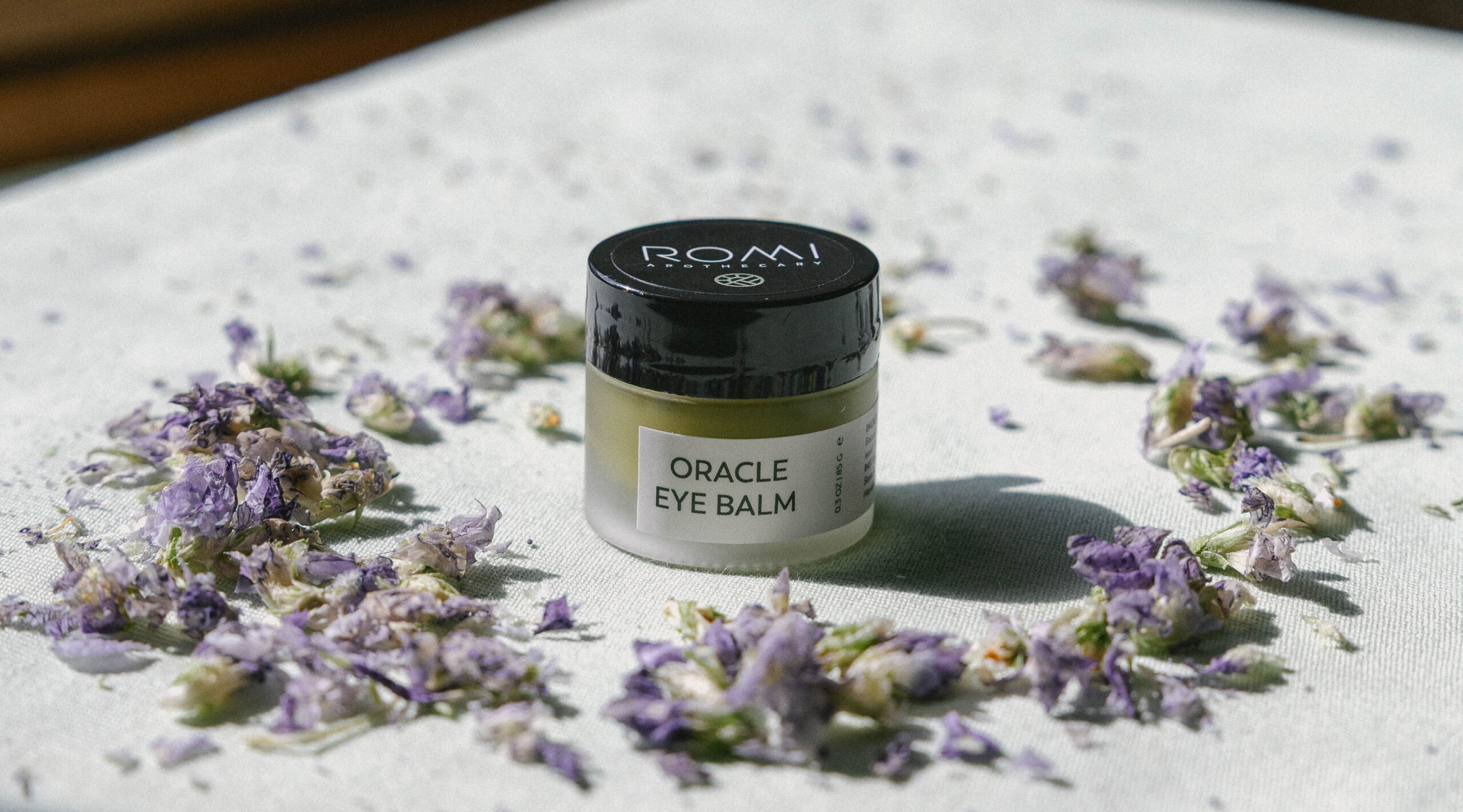 Wildcrafted violet flowers alongside Oracle Eye Balm, intimate and botanical