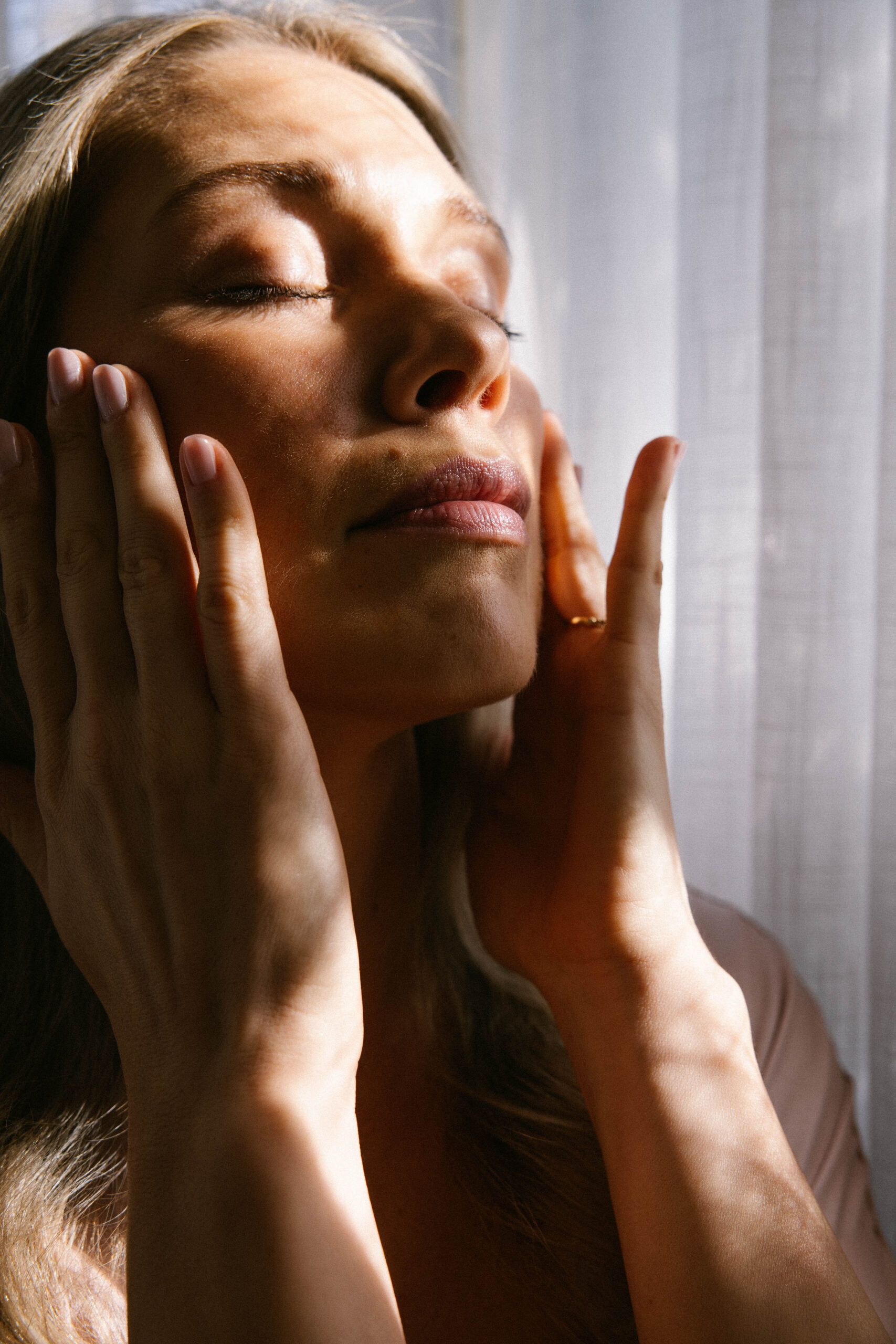 a woman in the soft morning light shining through a window after completing her morning skincare routine