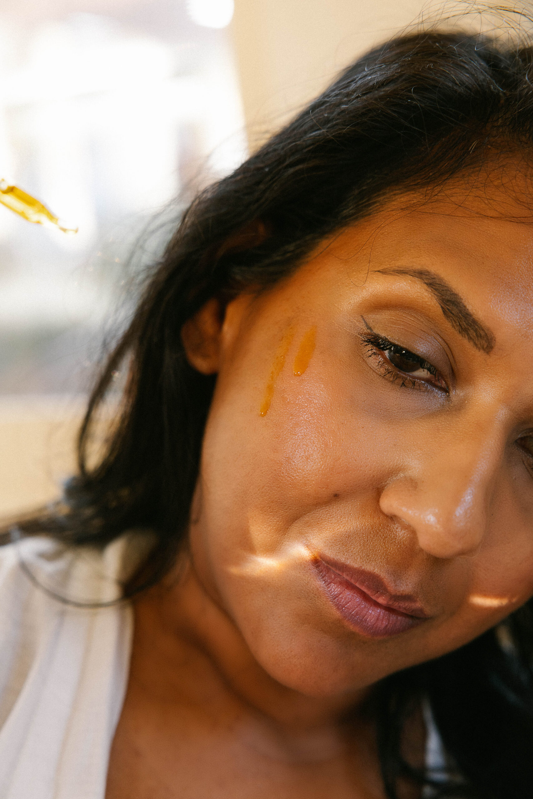 a woman putting drops of sunrise oil on her face as part of her morning skincare routine