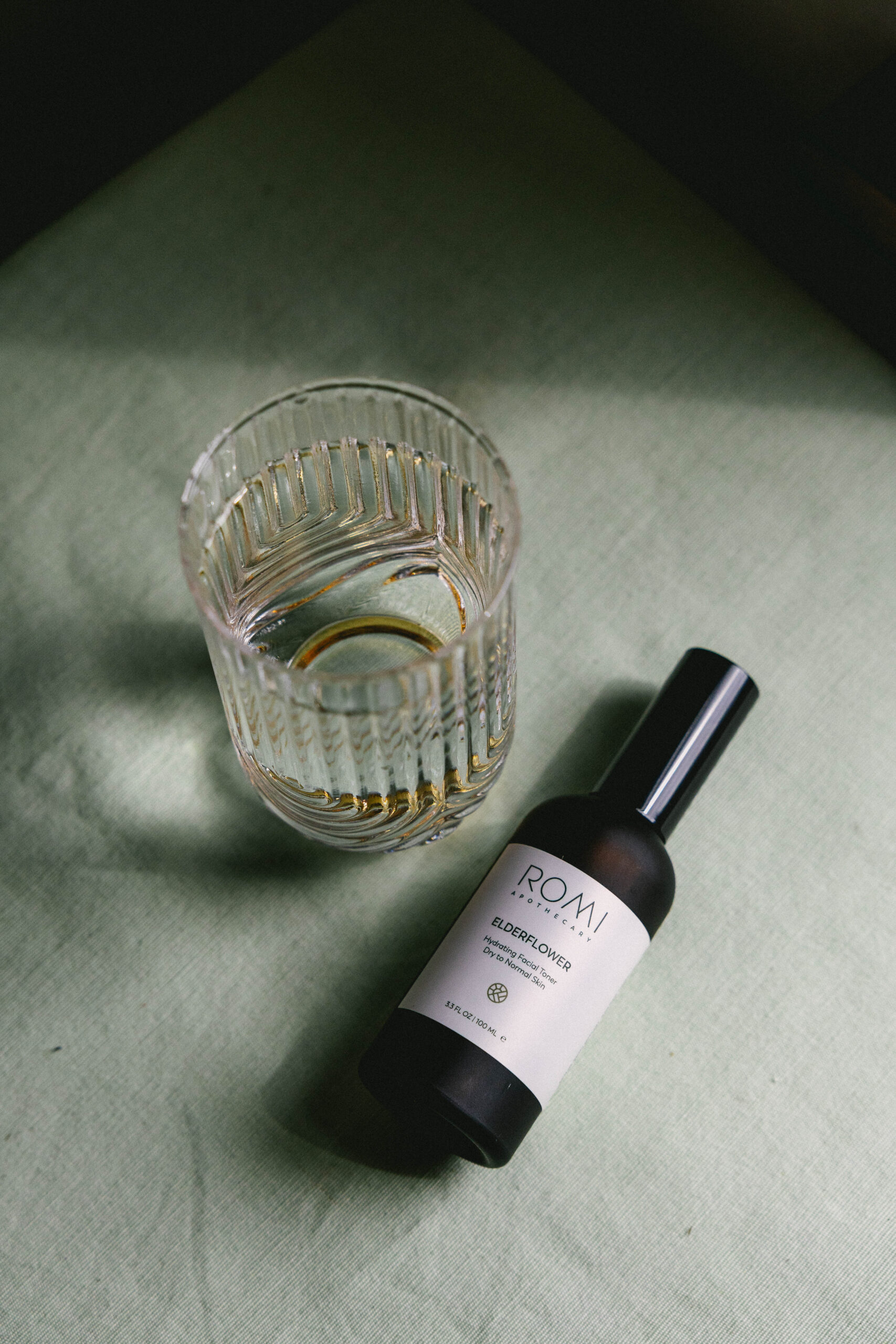 a glass of water next to a bottle of elderflower toner, water is an important aspect of a morning skincare routine